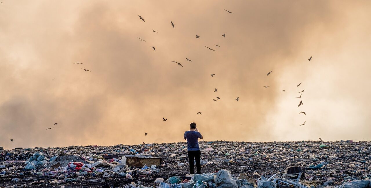 Man standing in a landfill with smoke and birds flying around, likening the AI model collapse to radioactive contamination during nuclear testing.